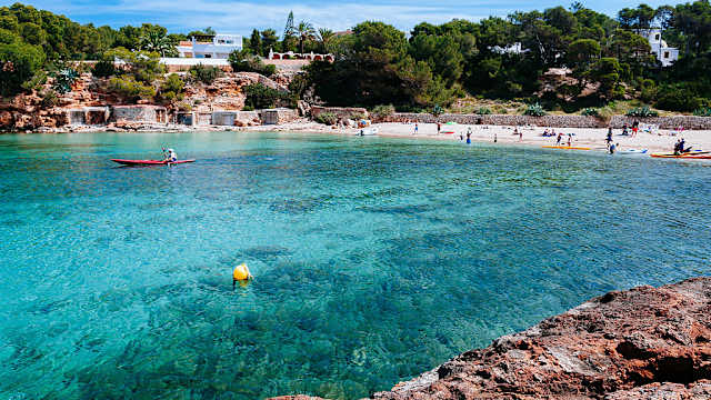 UrlauberInnen und KajakfahrerInnen im Meer und am Strand Cala Gració, Ibiza.