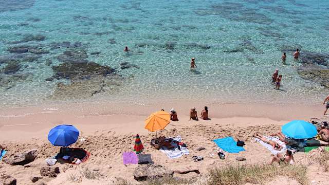 Blick von oben auf Strand von Ibiza mit Sonnenschirmen und Badegästen