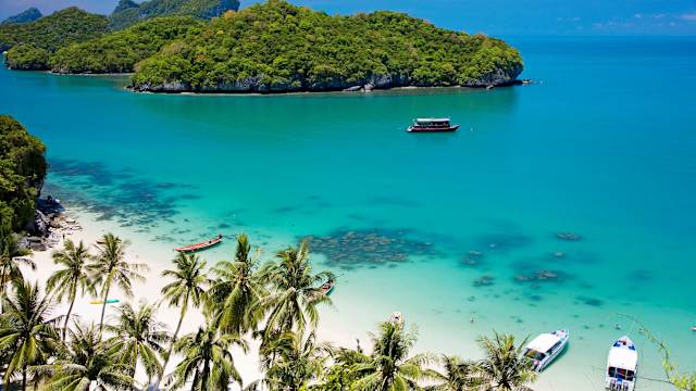 Boote am Strand auf Koh Samui mit Palmen und vorgelagerter Insel in Thailand