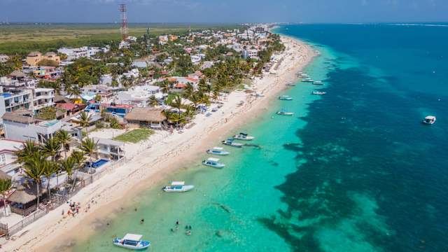 Boote und TouristInnen am Strand mit Palmen