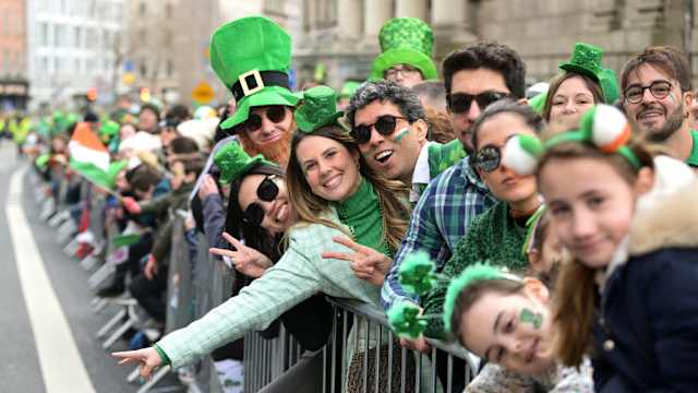 Menschen stehen verkleidet hinter einer Absperrung bei der St. Patrick's Day Parade in Irland.