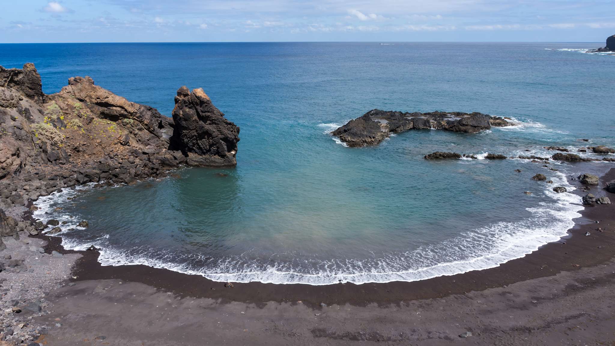 Der dunkle Strand befindet sich in einer geschützten, kleinen Bucht.