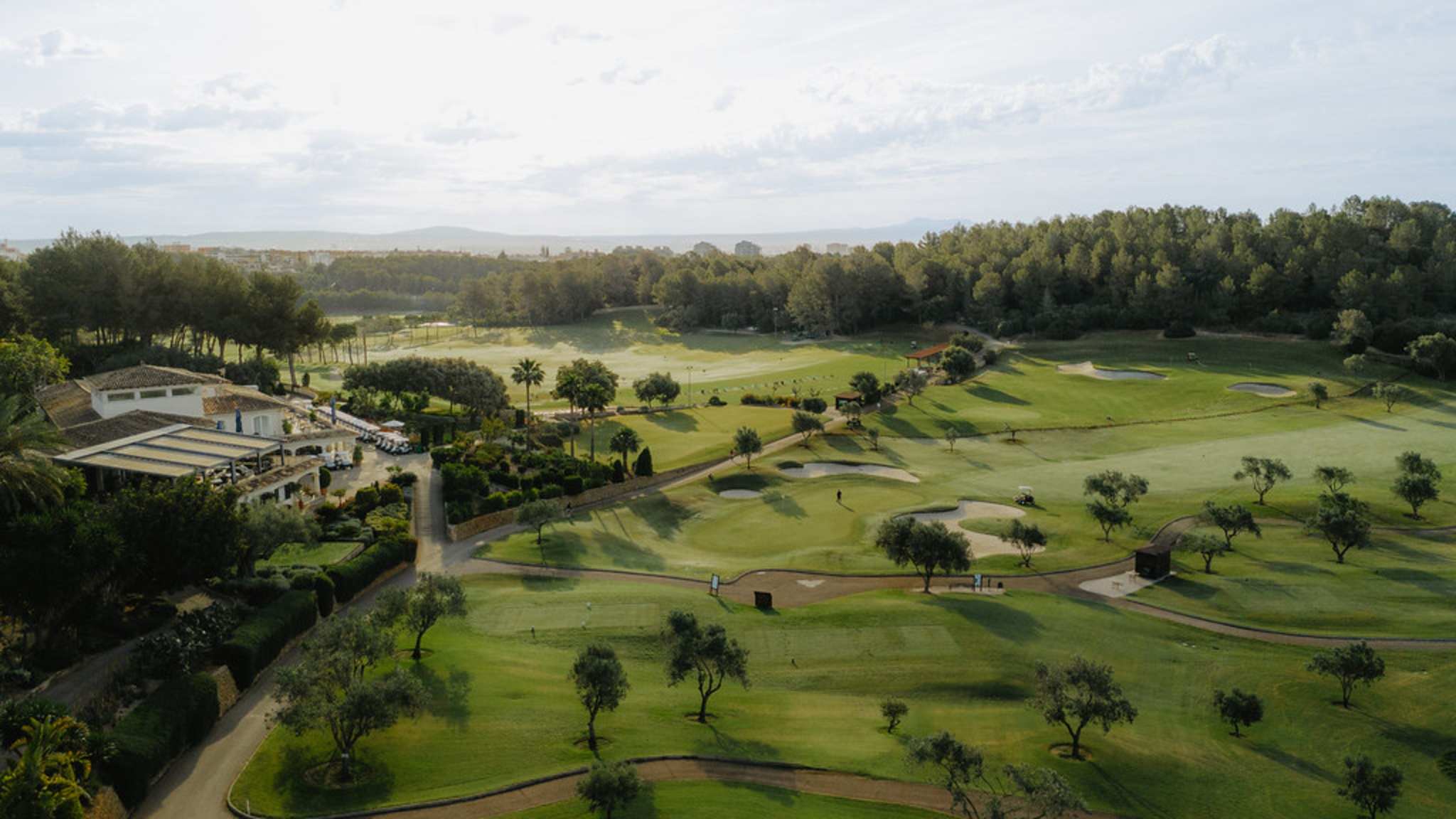Luftaufnahme eines Golfkurses aus der Luft, mit Meer und Bergen im Hintergrund.