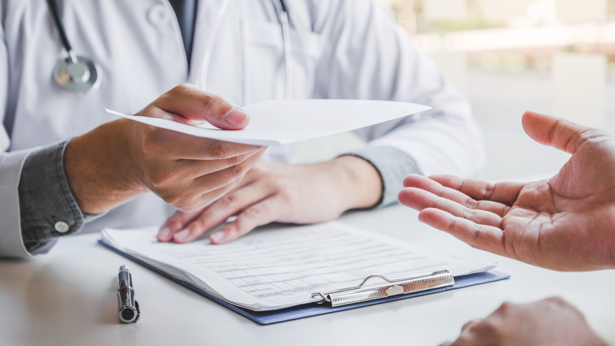 Arzt schreibt eine Diagnose und gibt ein ärztliches Rezept an einen Patienten ©iStock.com/SARINYAPINNGAM