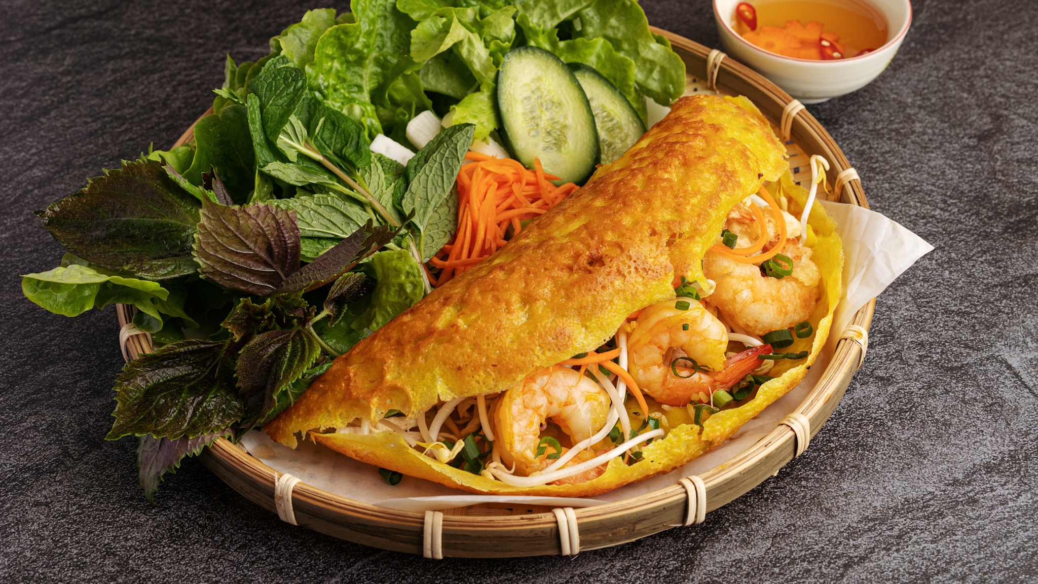 Ein Teller mit einem mit Garnelen und Sprossen gefüllten vietnamesischen Pfannkuchen mit einer Salat- und Kräuterbeilage.