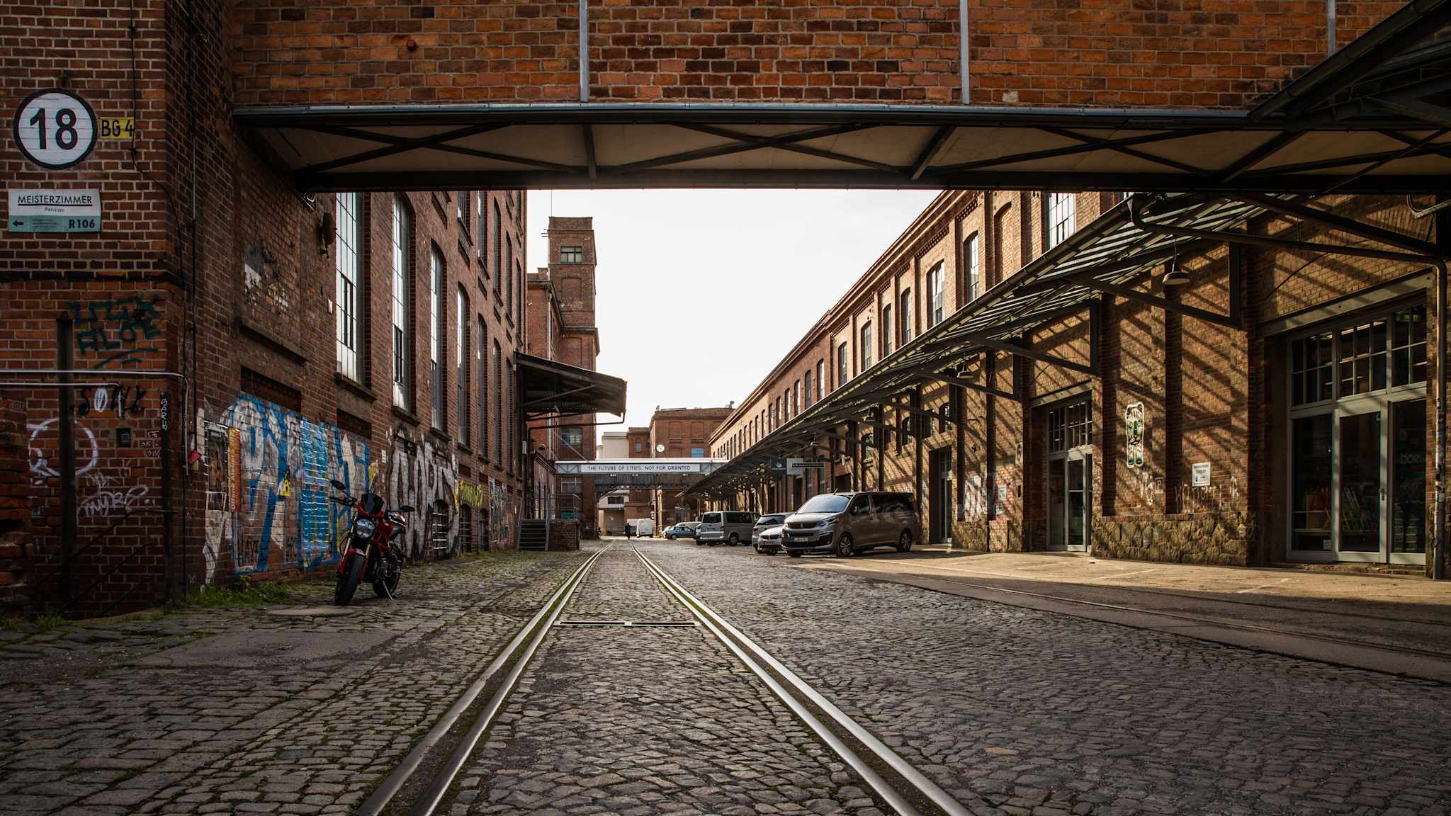 Blick auf eine Straße mit alten Gleisen durch die Backstein-Gebäude der alten Baumwollspinnerei in Leipzig.