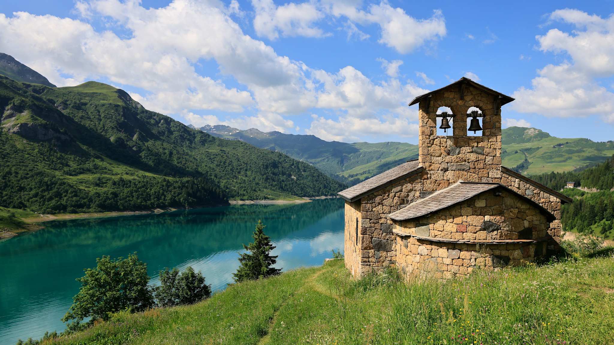 Eine kleine Kapelle aus Stein steht auf einem Berg mit Blick auf den See Lac de Roselend