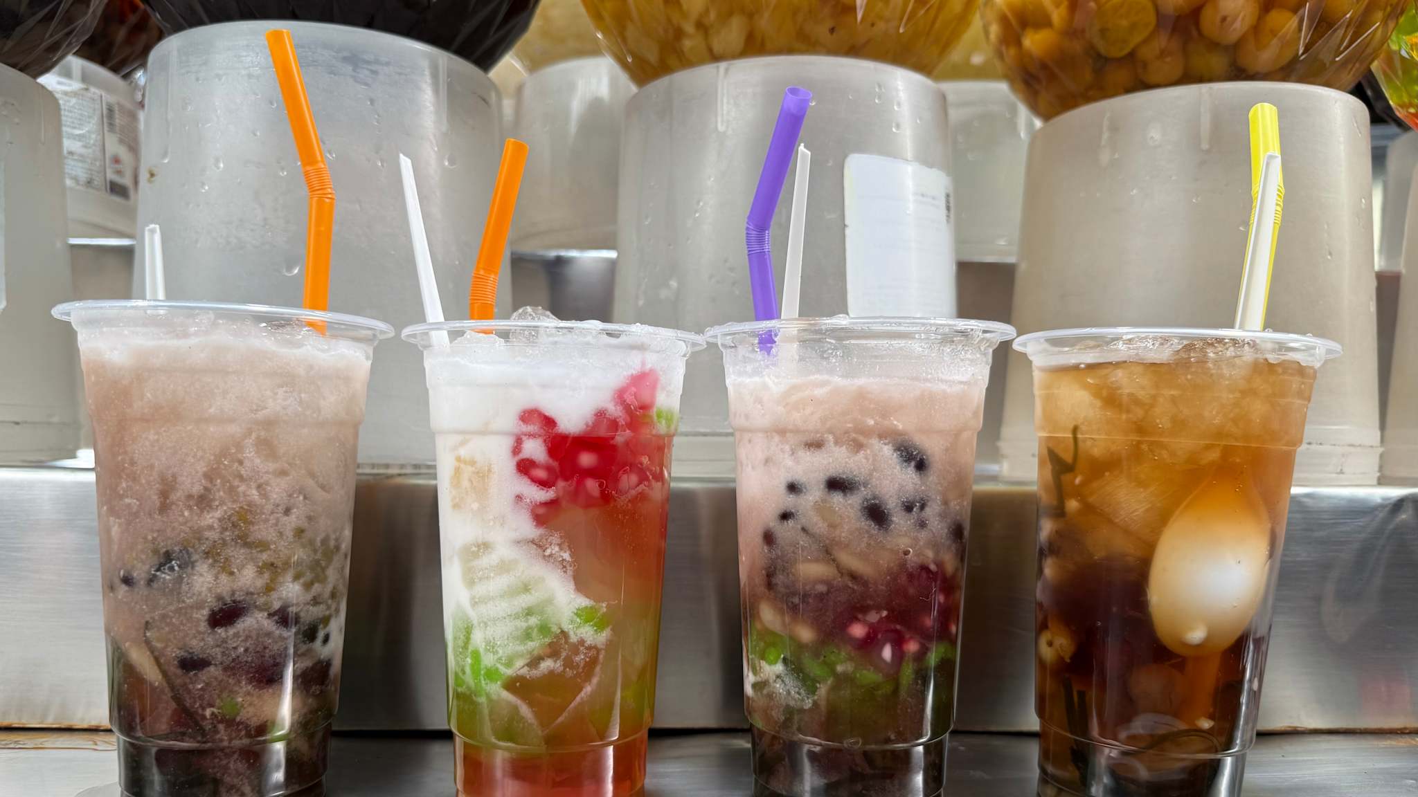 Vier durchsichtige Becher mit bunten Flüssigkeiten und Desserts.