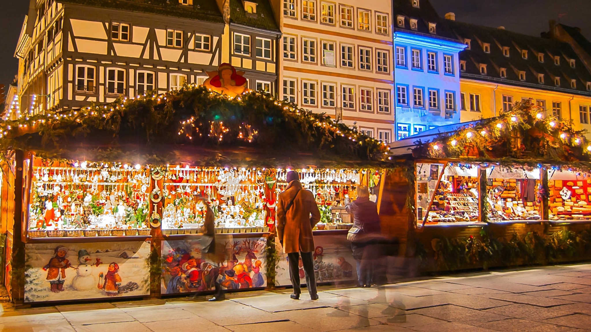 Weihnachtsmarkstände auf einem Platz in Straßburg umgeben von Menschen und weihnachtlicher Beleuchtung.