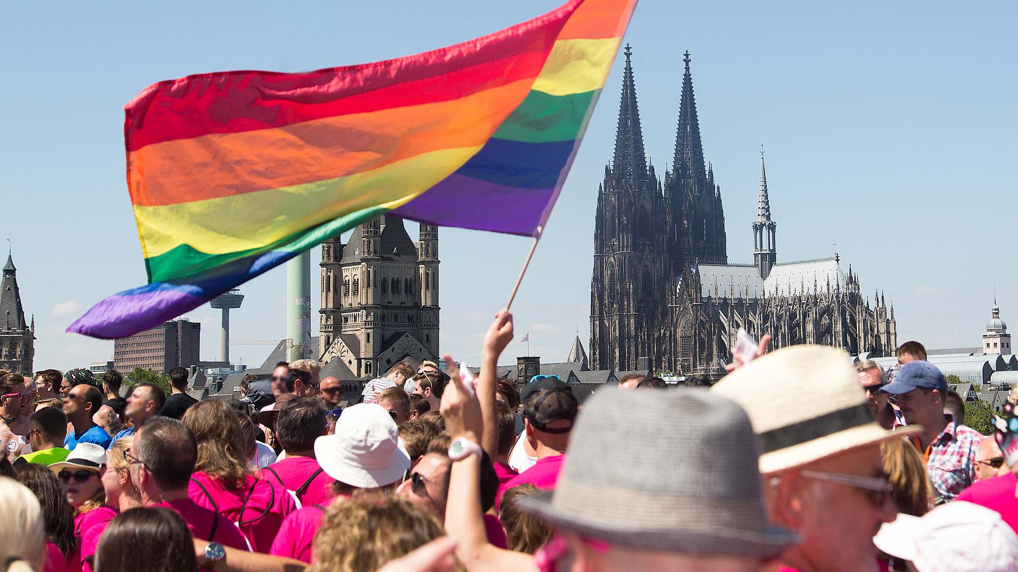 Menschenmenge mit großer Regenbogenflagge in der Nähe des Kölner Doms