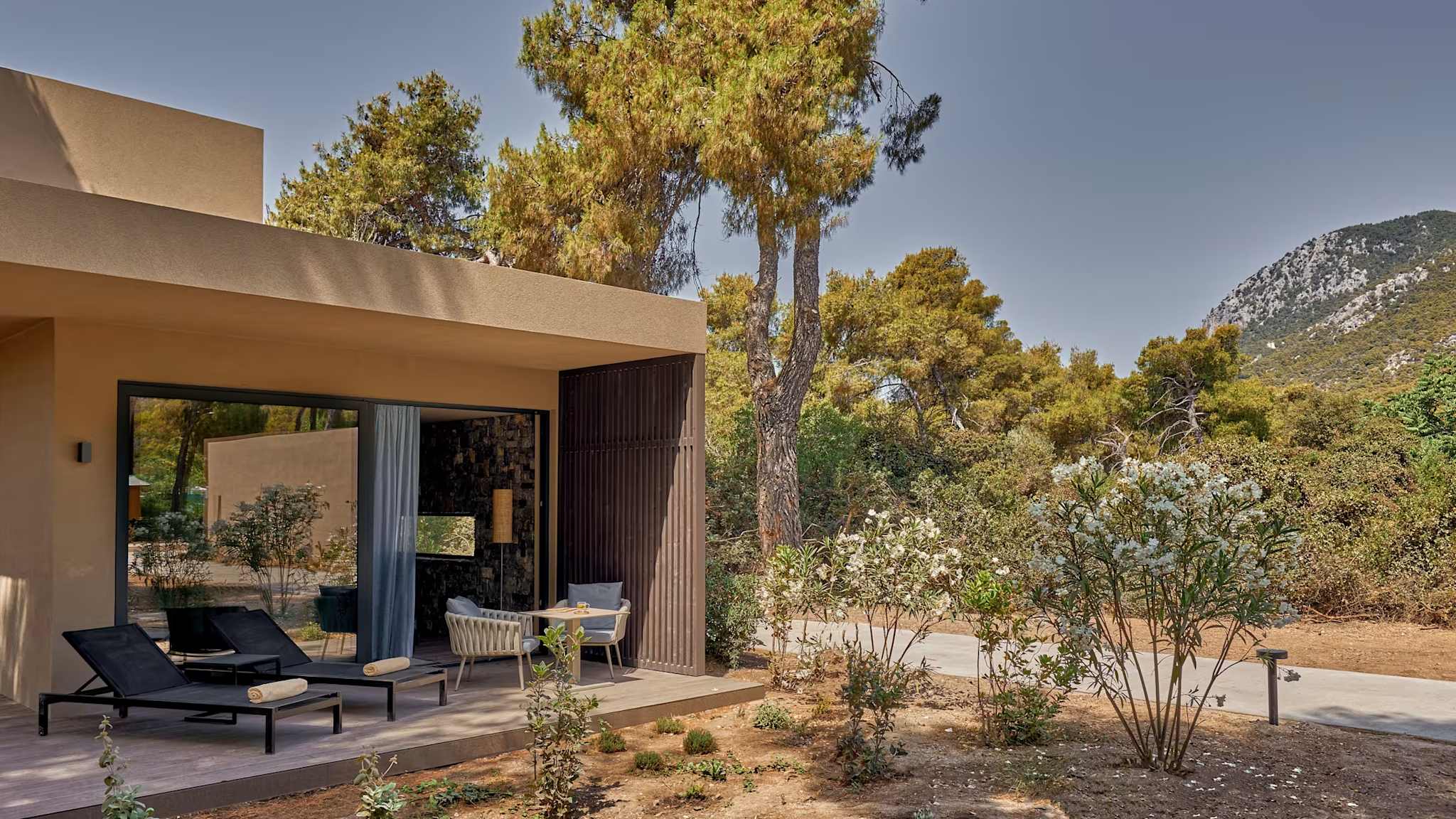 Blick auf eine Terrasse eines Hotelzimmers, mit zwei bereitstehenden Liegen und zwei Stühlen.