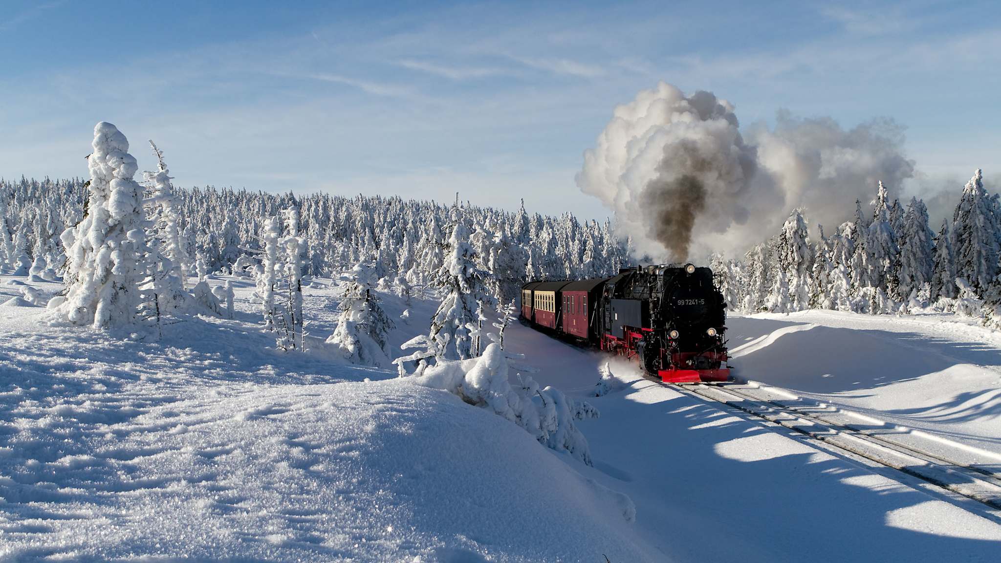 Eine schwarze Dampflok fährt durch eine tief verschneite Landschaft im Harz, umgeben von schneebedeckten Bäumen.