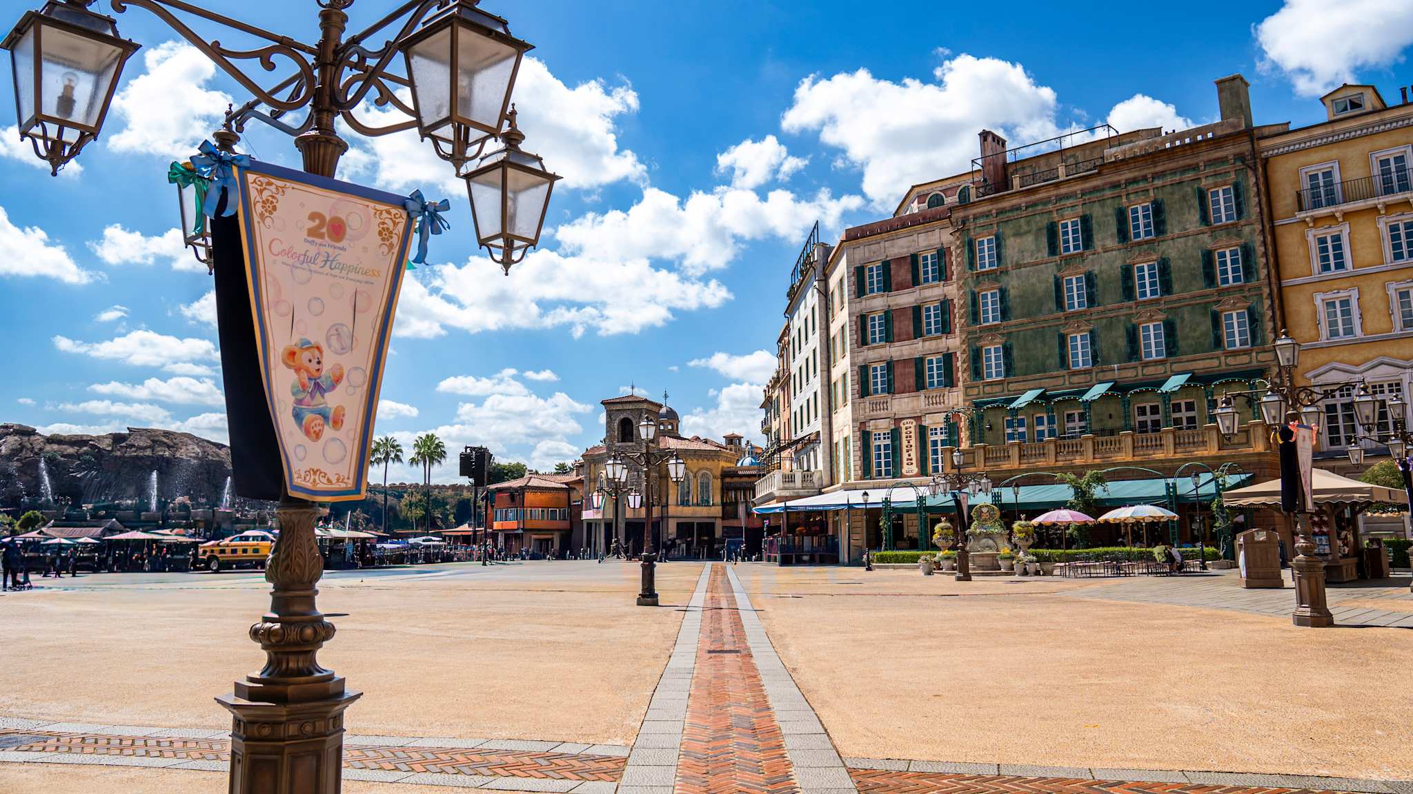 Ein Platz mit bunten, ästhetischen Häusern am Rand, einer verschnörkelten Laterne im Vordergrund und im Hintergrund Berge mit kleinen Wasserfällen im DisneySea bei Tokyo, Japan.