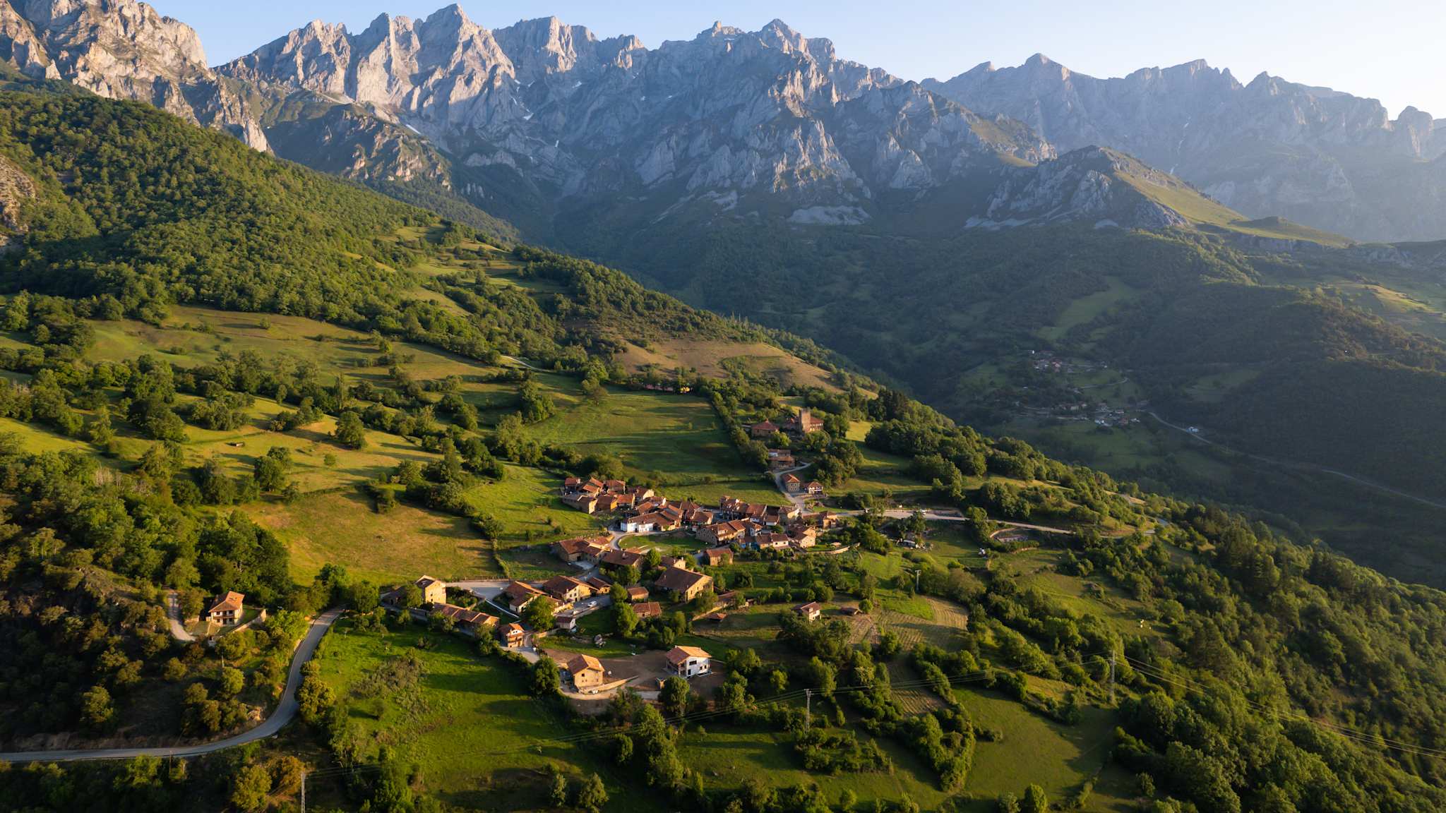 Ein Dorf liegt auf einem großen Hügel. Hinter dem Hügel erheben sich hohe Berge.