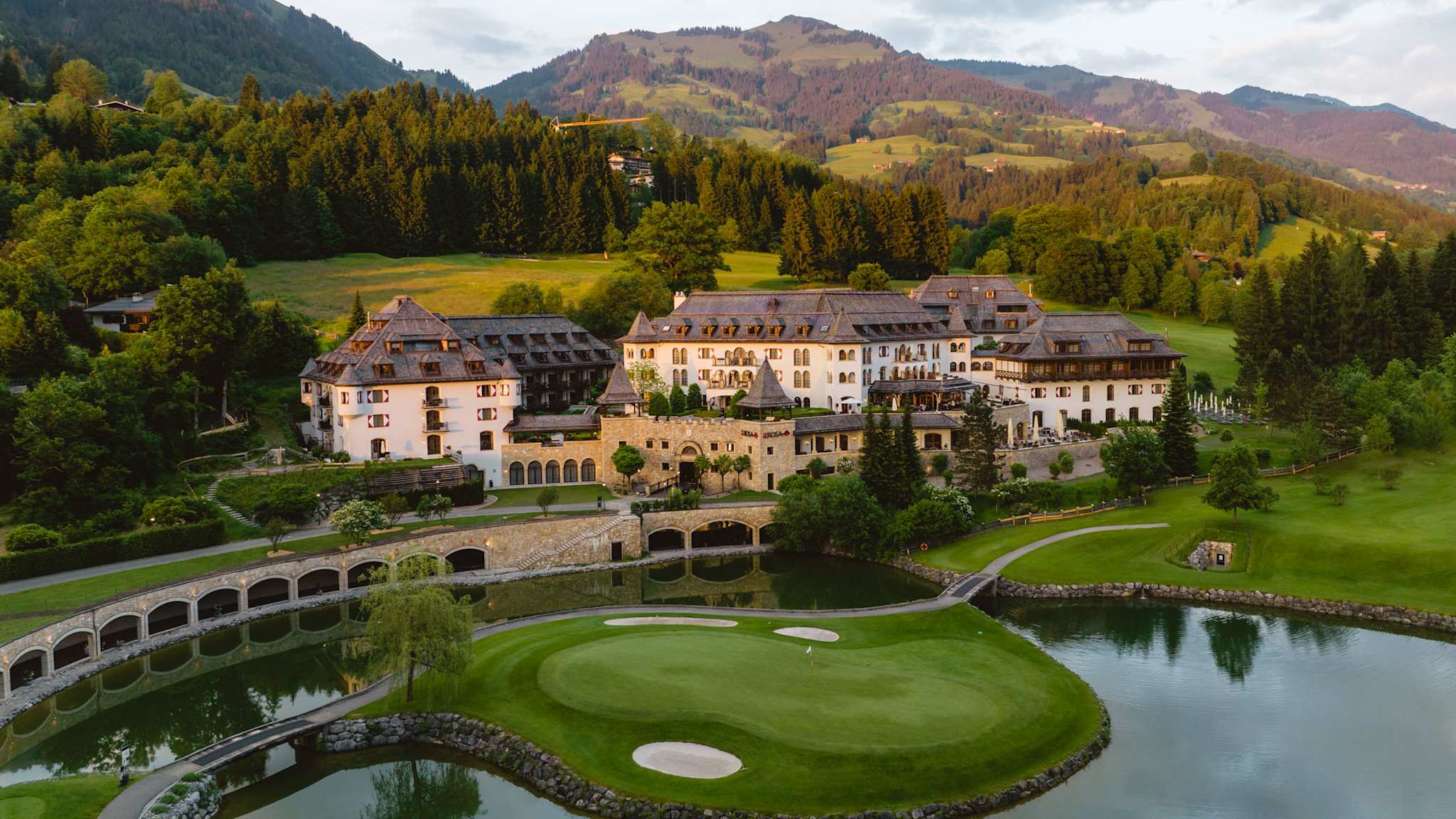 Außenansicht des Schlosshotel Kitzbühel mit Türmchen, See und umliegender Berglandschaft in Tirol.