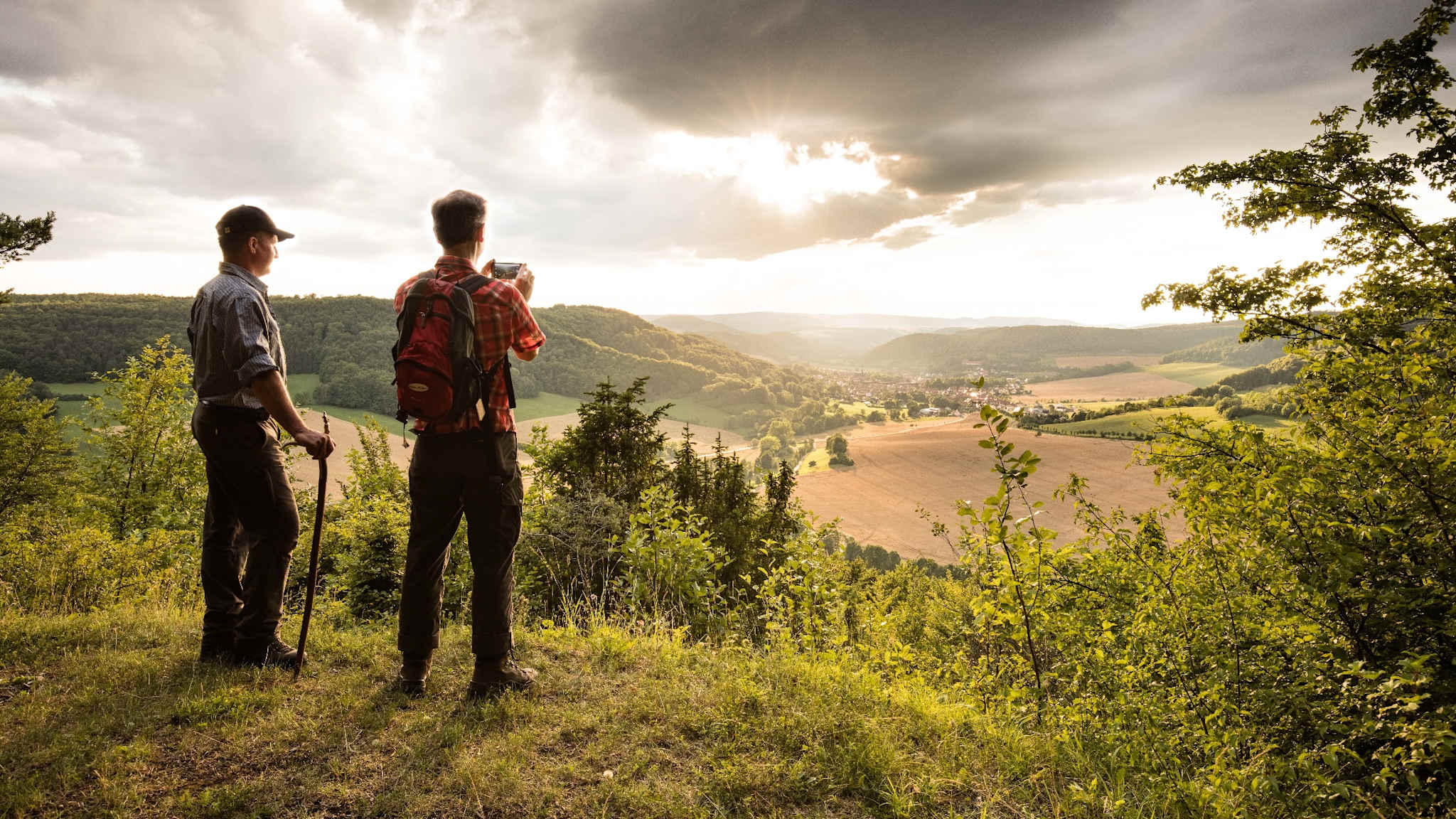 Zwei Männer blicken auf ein Tal bei Sonnenuntergang