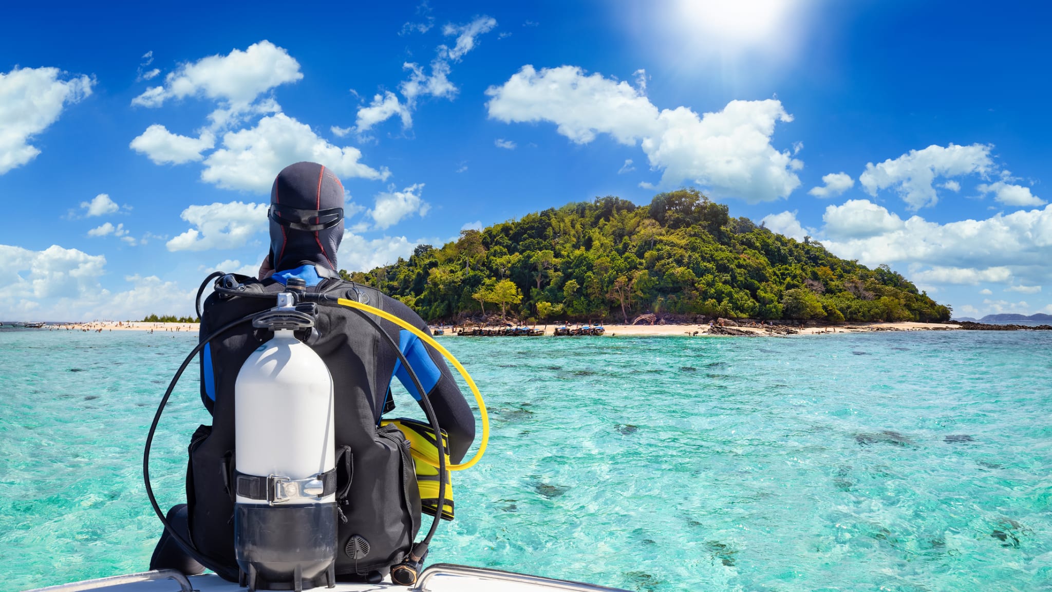 Ein Taucher auf einem Boot und blickt auf das türkisfarbene Meer © iStock.com/SHansche