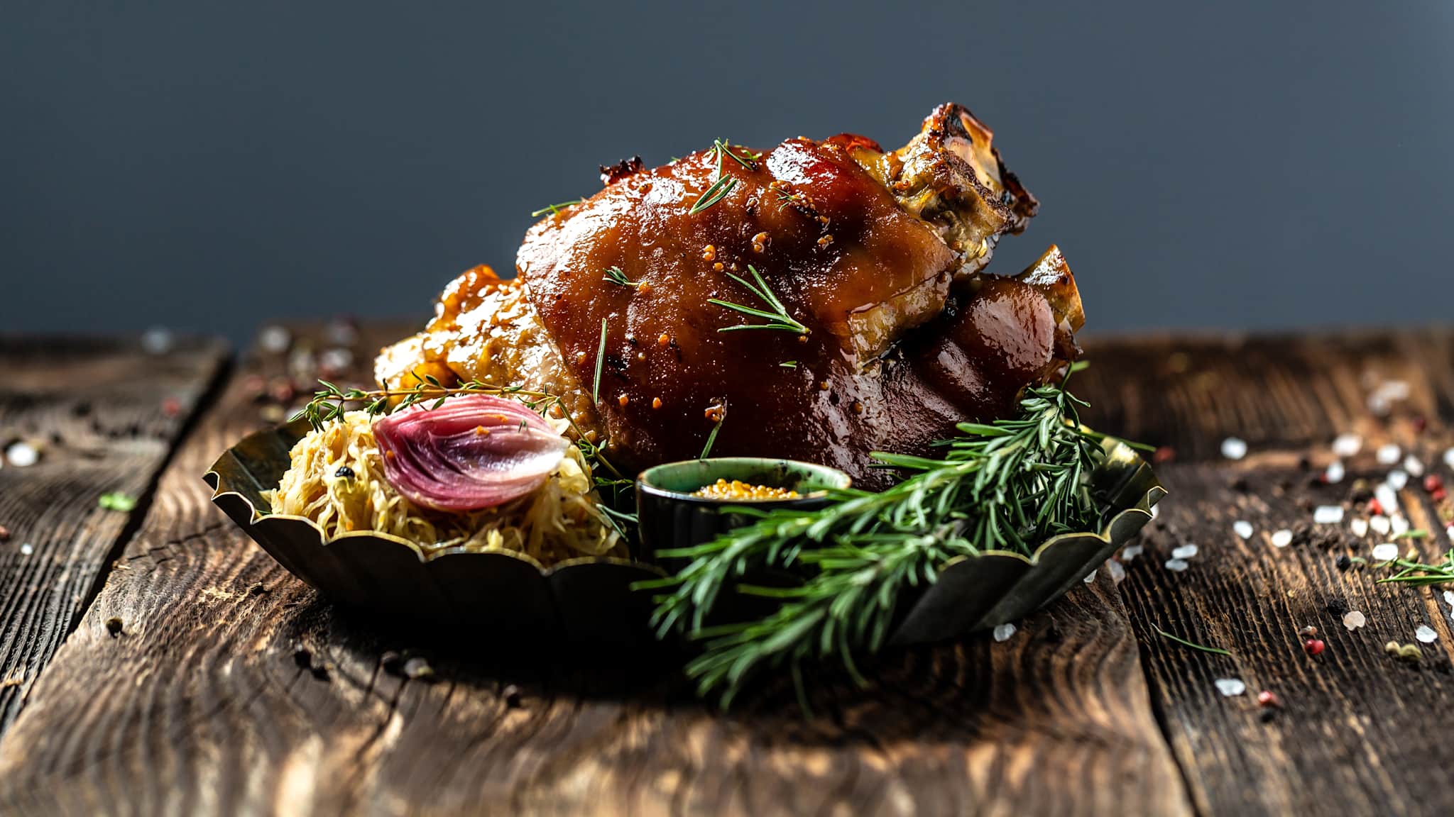 Zartes Eisbein mit Kraut und Senf in einer Schale mit Rosmarin auf einem rustikalen Tisch.