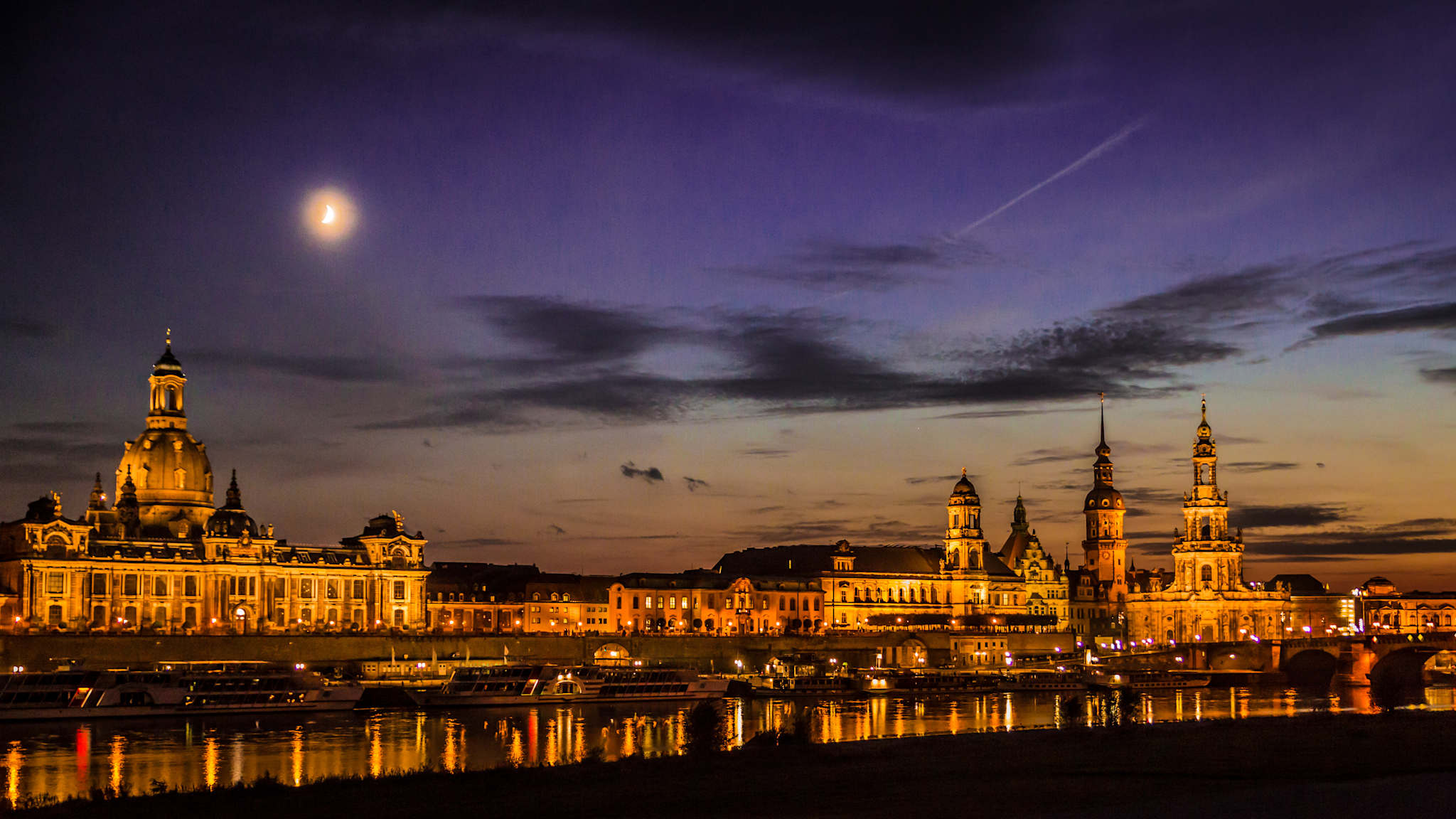 Flussufer mit beleuchteten, barocken Gebäuden am Abend