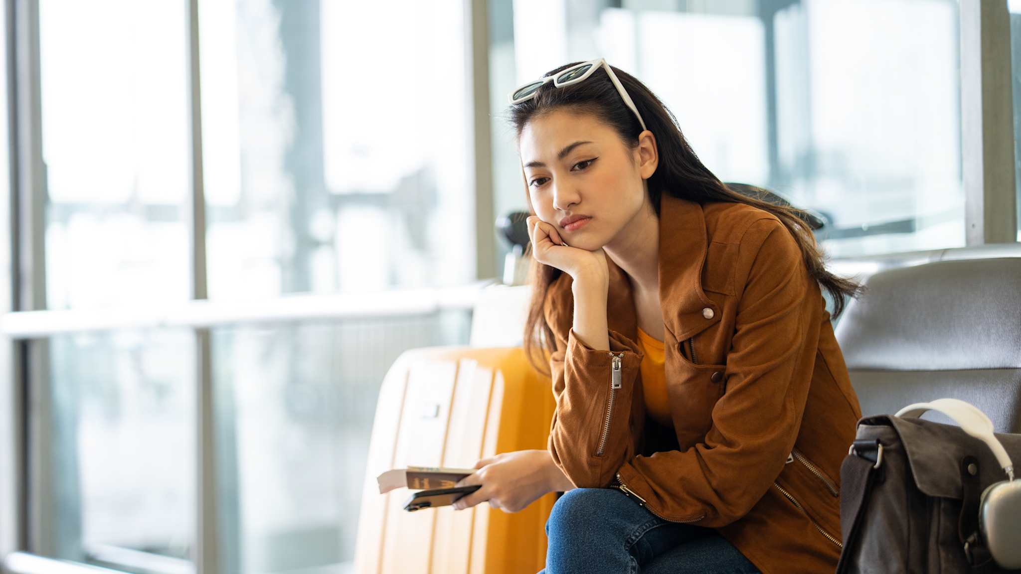 Eine enttäuscht wirkende Urlauberin sitzt im Flughafen und stützt den Kopf auf eine Hand