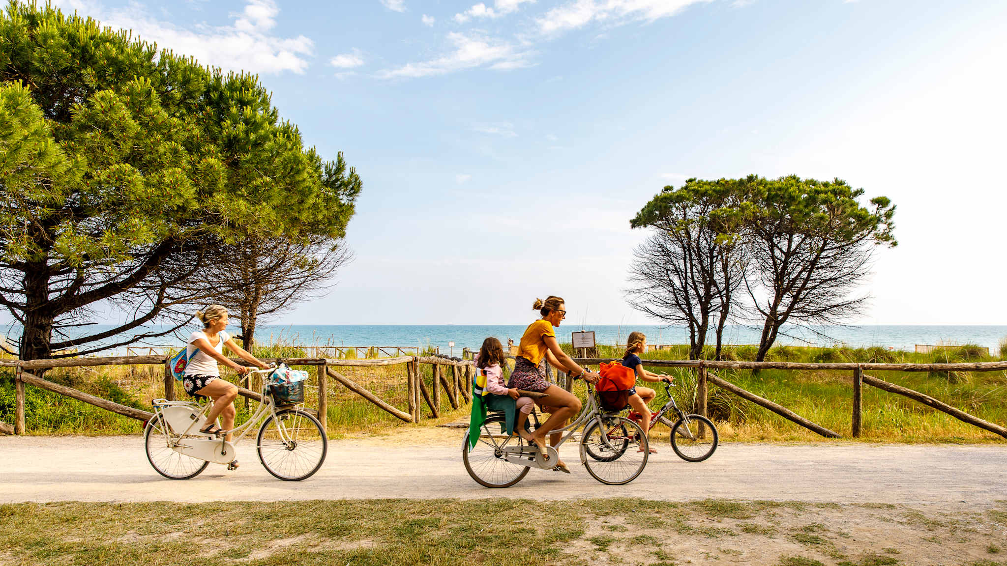 Eine Familie mit zwei Kindern fährt auf Fahrrädern vor den Dünen am Meer entland.