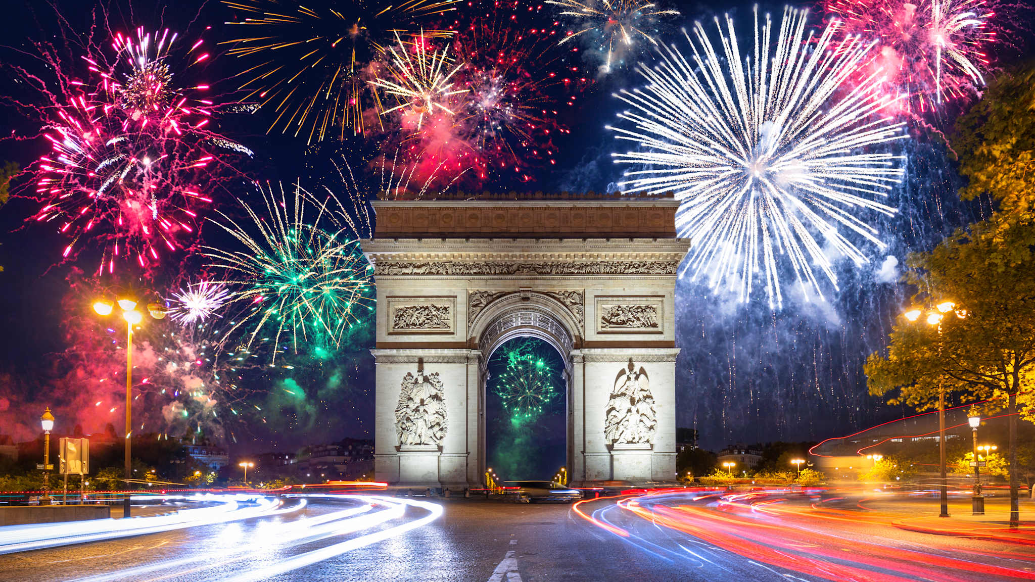 Der Arc de Triomphe in Paris vor einem dunklen Himmel voller Feuerwerk.
