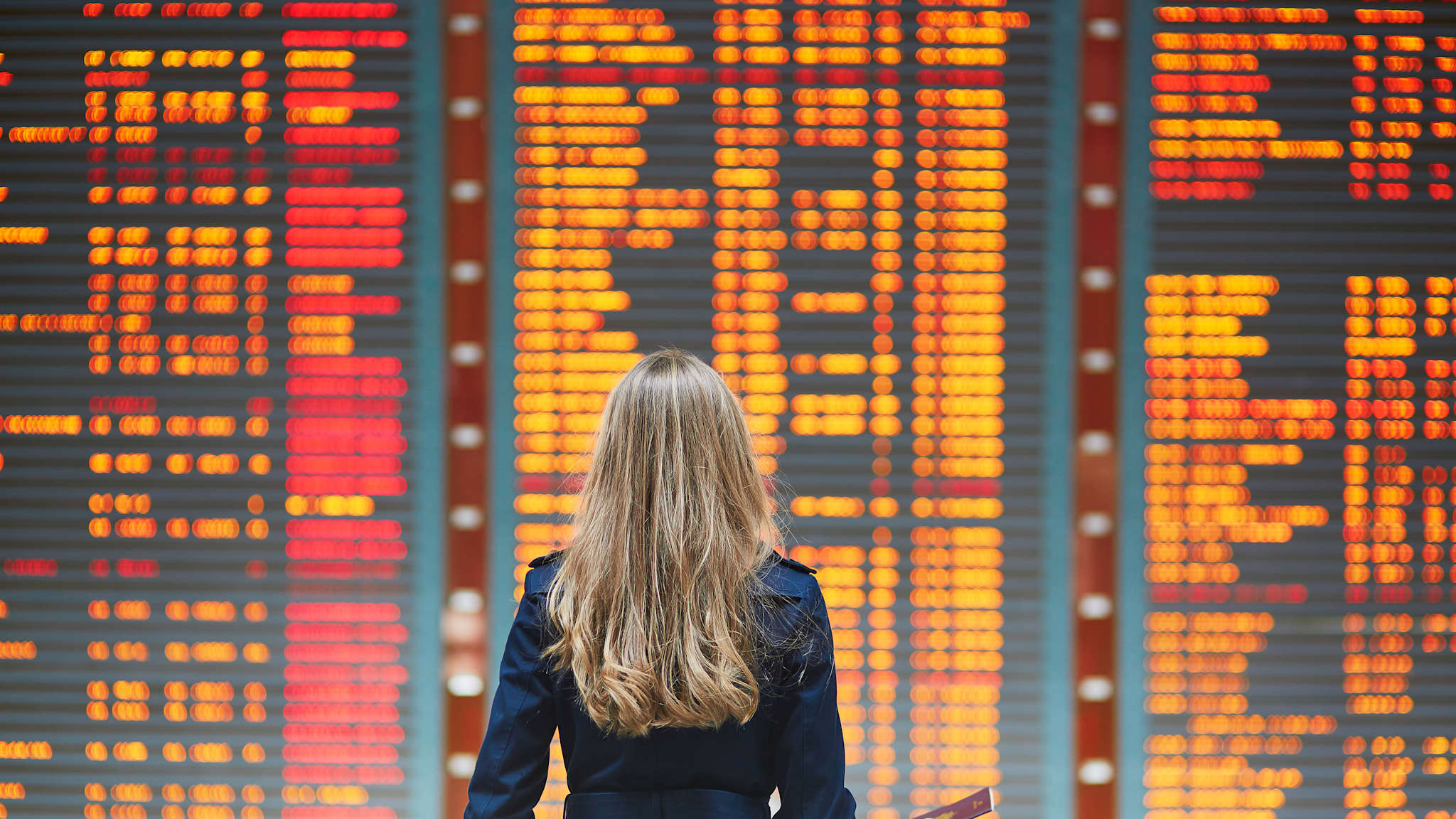 Frau steht vor einer Anzeigetafel mit Flügen im Flughafen