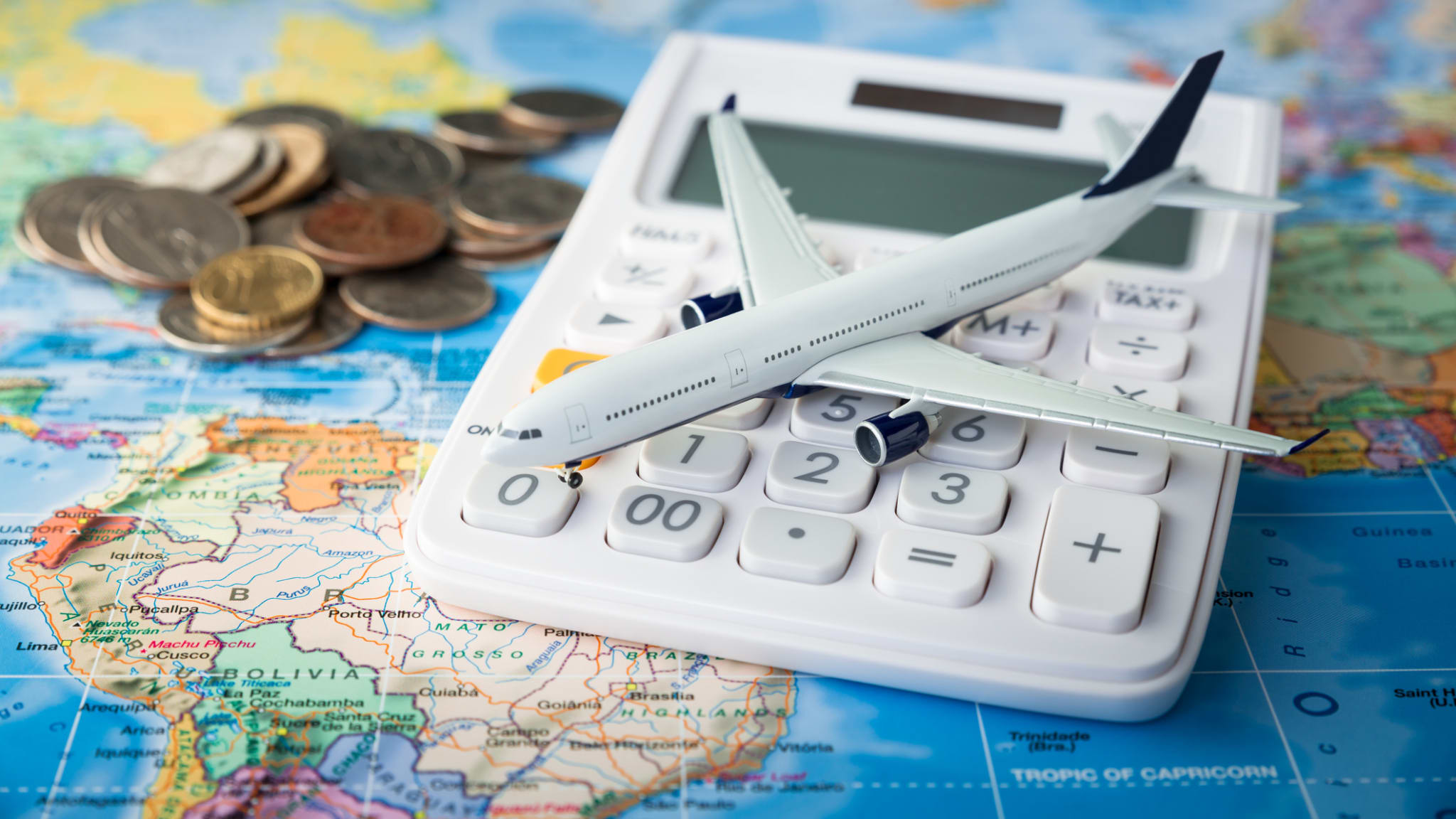 Flugzeug auf einem Taschnerechner mit Kleingeld auf einer Weltkarte © iStock.com/Sezeryadigar