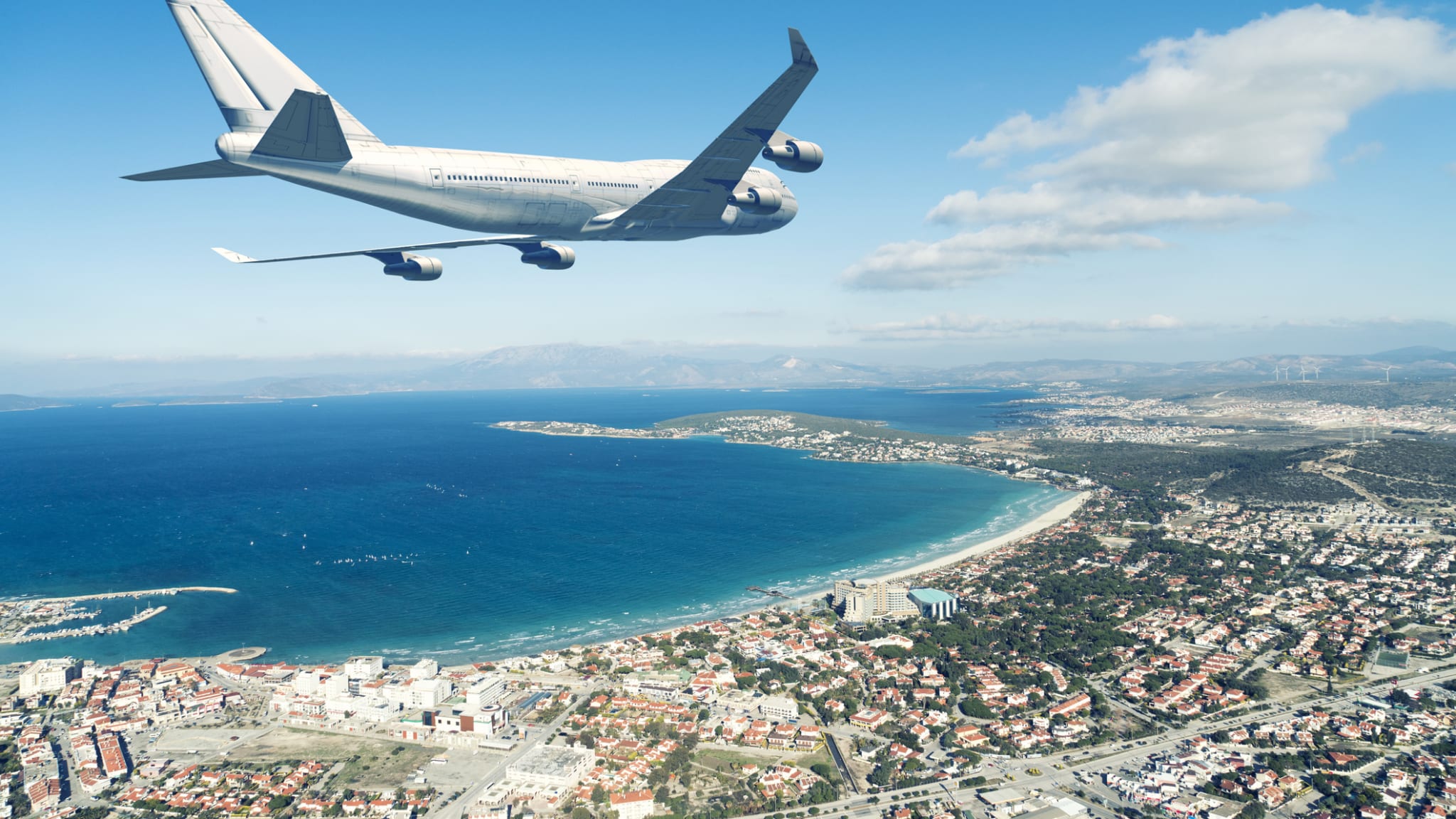 Flugzeug fliegt über eine Küstenstadt an blauem Himmel © iStock.com/jpgfactory