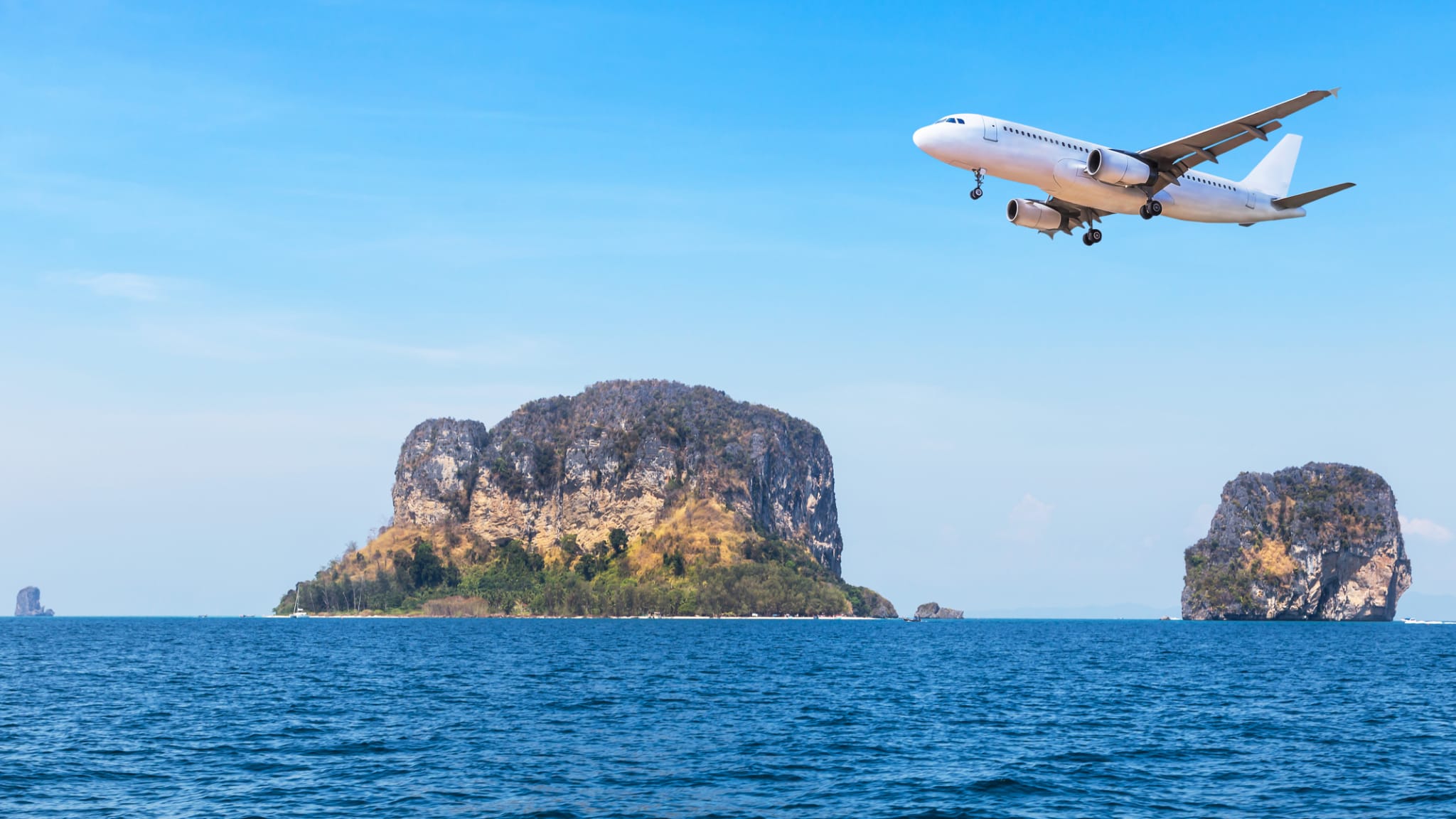 Flugzeug fliegt über eine kleine Insel auf blauem Meer ©Airubon/iStock