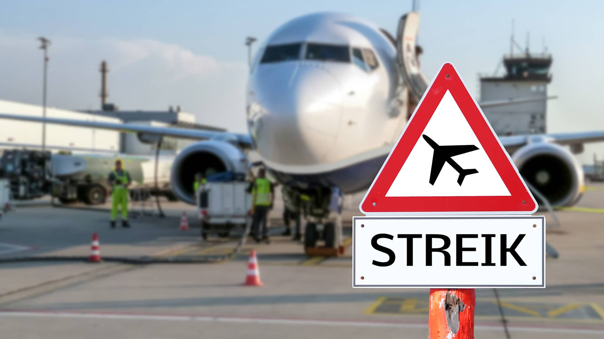 Ein Warnschild mit der Aufschrift „Streik“ vor einem Flugzeug am Flughafen symbolisiert Flugausfälle und die Frage nach Entschädigungsansprüchen der Passagiere.