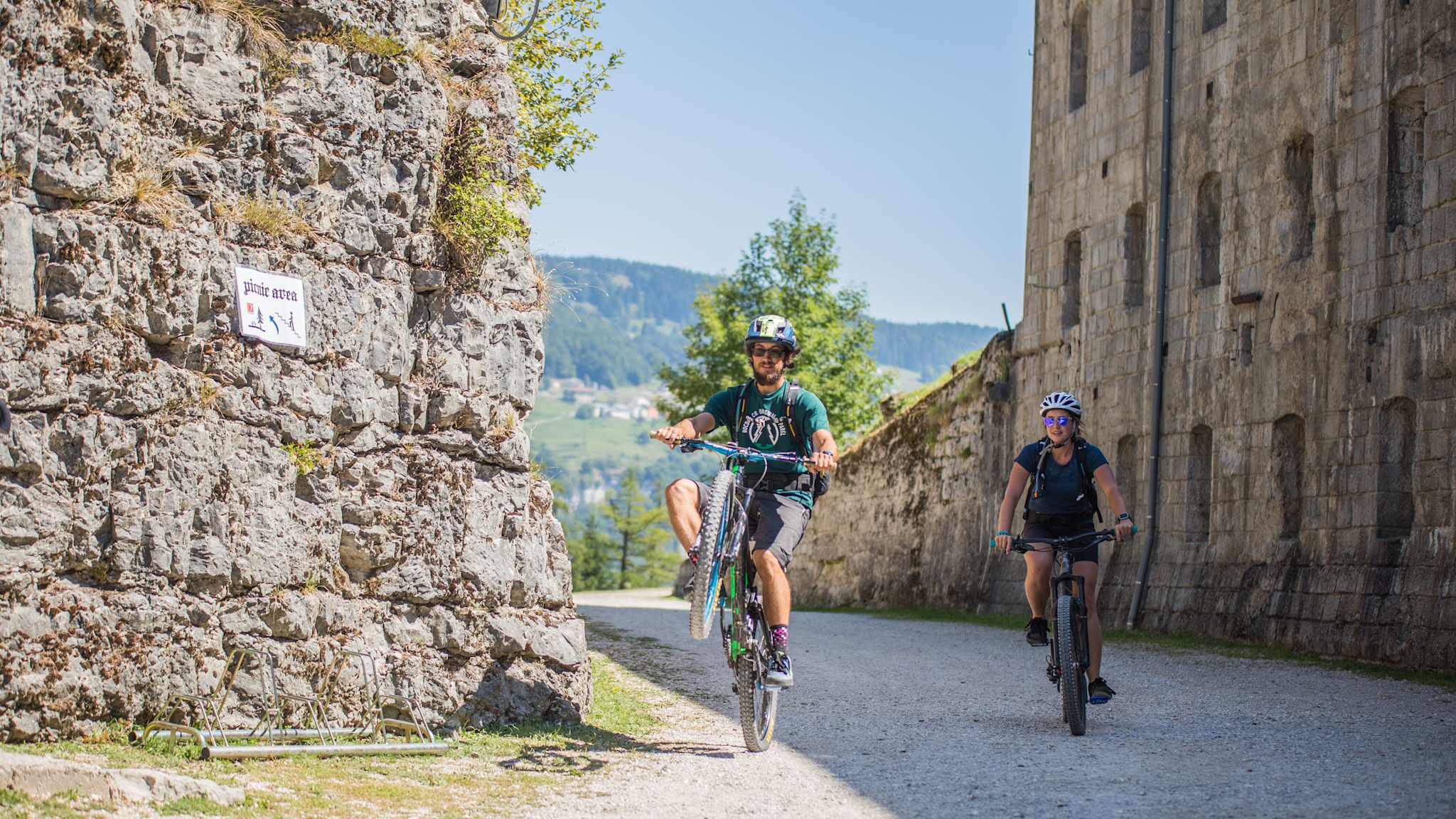Zwei Radfahrer erkunden eine Festung und fahren zwischen den Gebäuden entlang