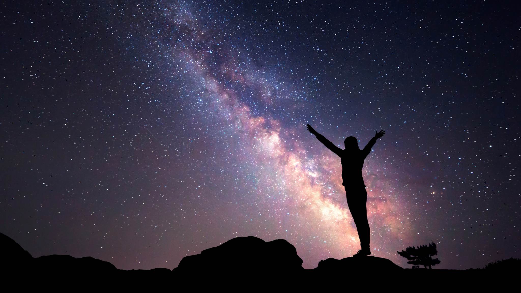 Frau streckt vor einem Sternenhimmel mit Milchstraße die Arme in die Luft
