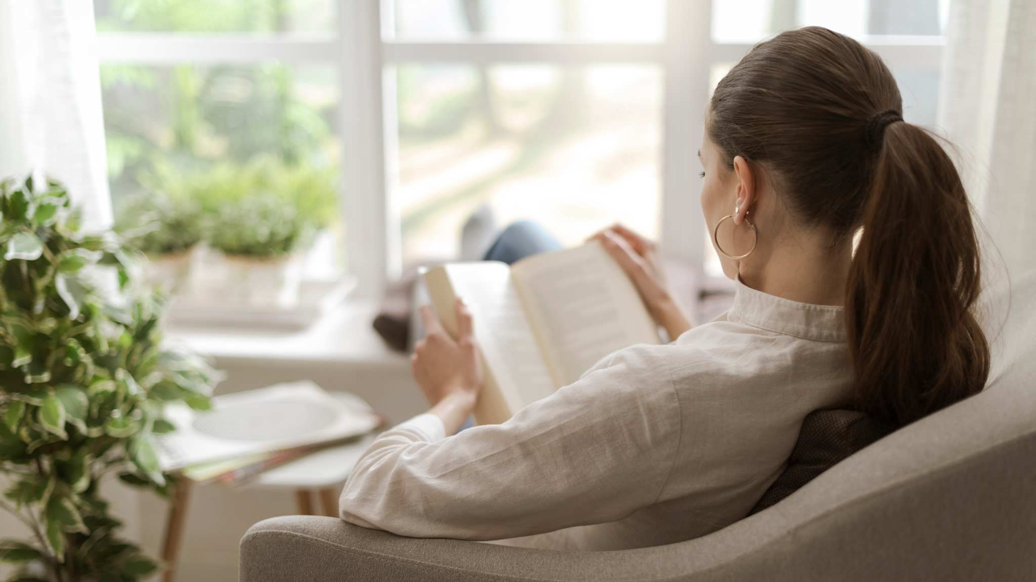 Blick von der Seite auf eine Frau, die mit hochgelegten Beinen in einem Sessel sitzt und ein Buch liest