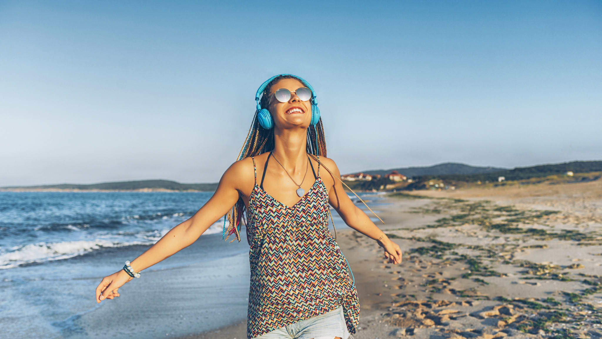 Fröhliche junge Frau hört Musik mit Kopfhörern am Strand © iStock.com/Vladimir Vladimirov