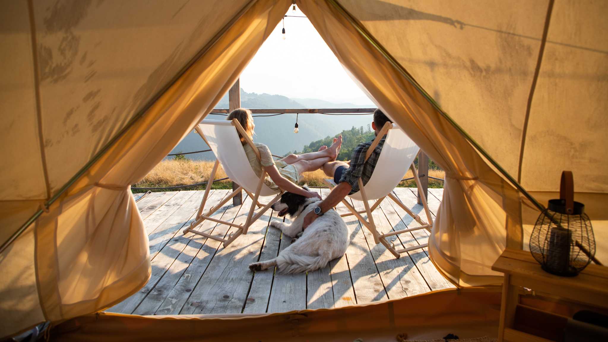 Ein Paar sitzt mit Hund auf der Terrasse eines Glamping-Zelts