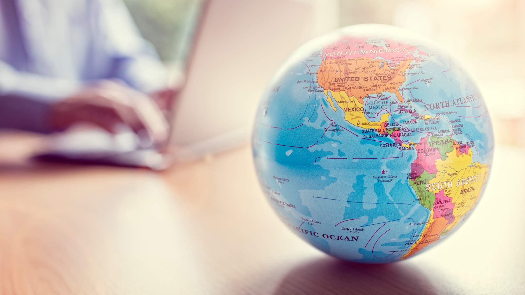 Ein Globus-Ball liegt auf einem Tisch mit einem Laptop im Hintergrund.