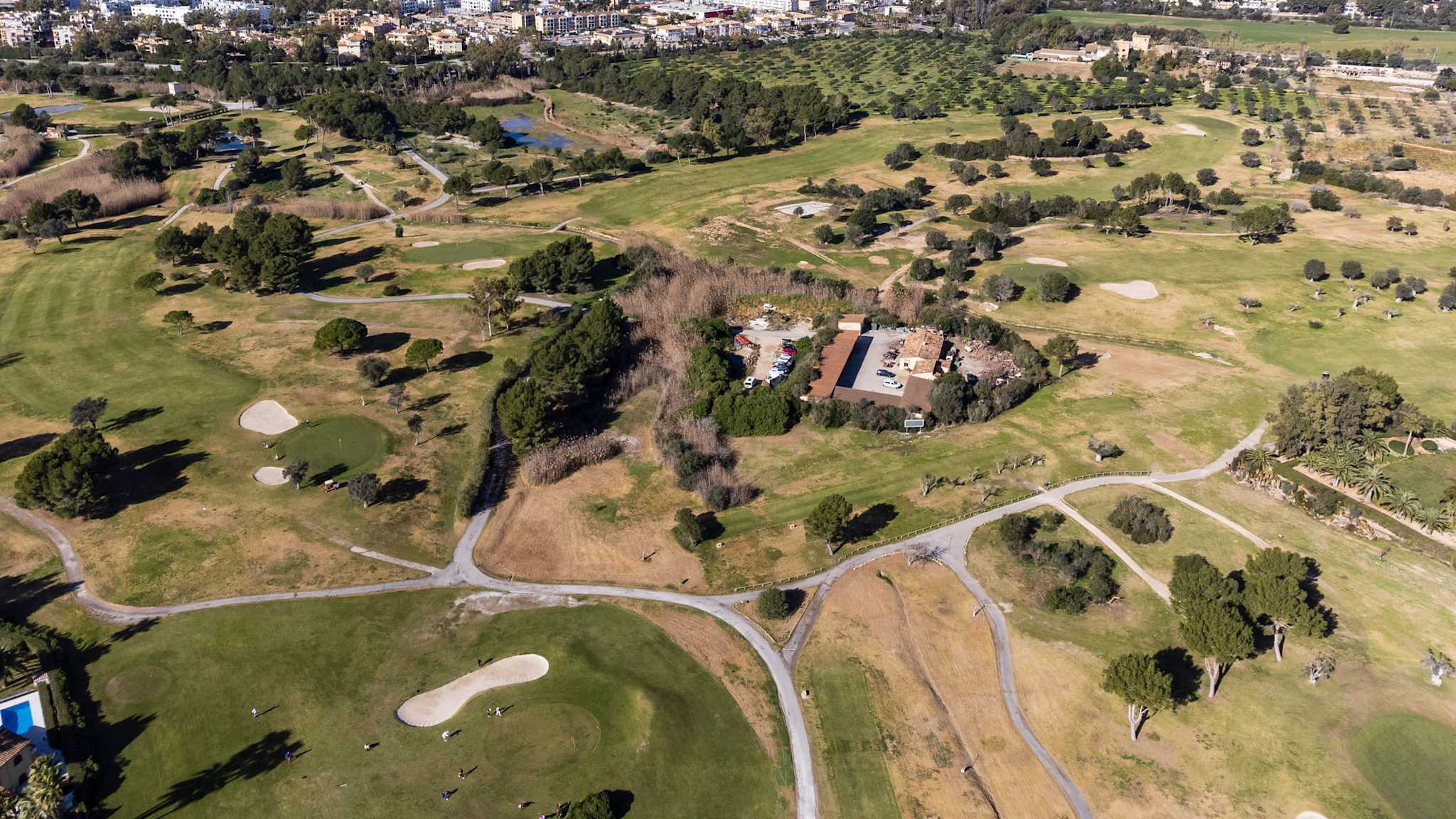 Luftaufnahme eines weitläufigen Golfplatzes auf Mallorca mit Blick auf die Küste, umliegende Wohngebiete und grüne Fairways.