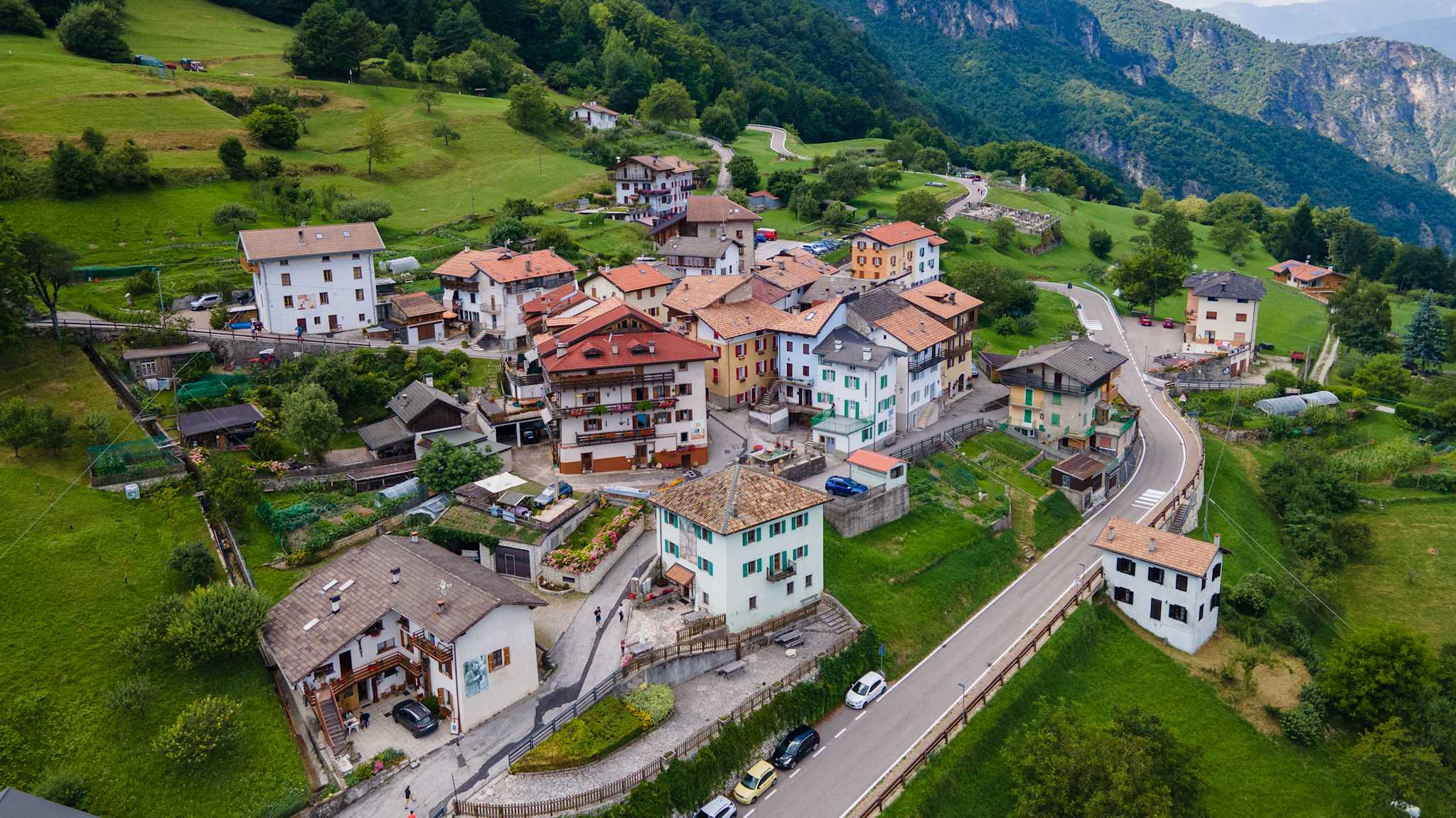 Luftansicht auf ein kleines Dorf in den Alpen. Die Häuser sind mit aufwändigen Wandmalereien geschmückt.