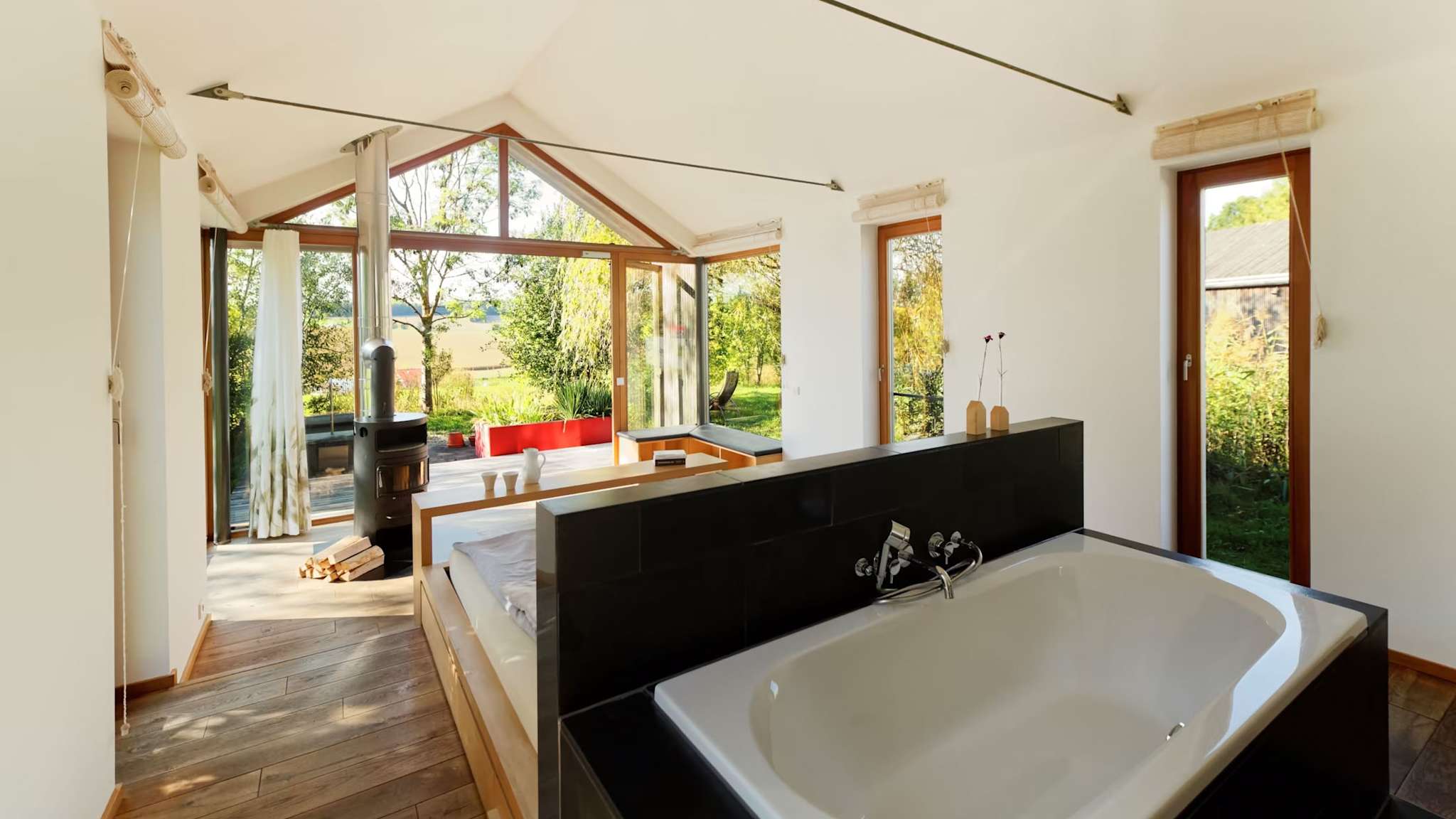 Innenraum im Hofgut Hafnerleiten mit Badewanne, Bett, Holzofen und großen Glasfronten.