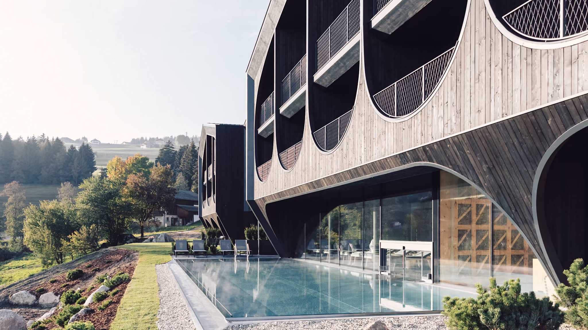 Außenansicht des Hotels Milla Montis in Meransen mit Pool, moderner Holzfassade und Berglandschaft im Hintergrund.