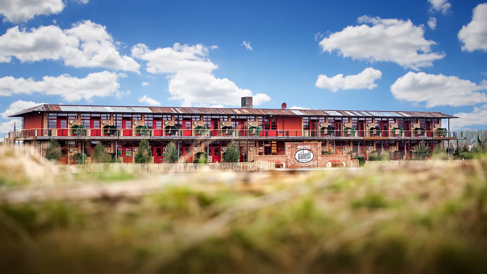Außenanischt eines zweigeschossigen Hotels mit roter Wandfarbe, zwischen Wiesen gelegen