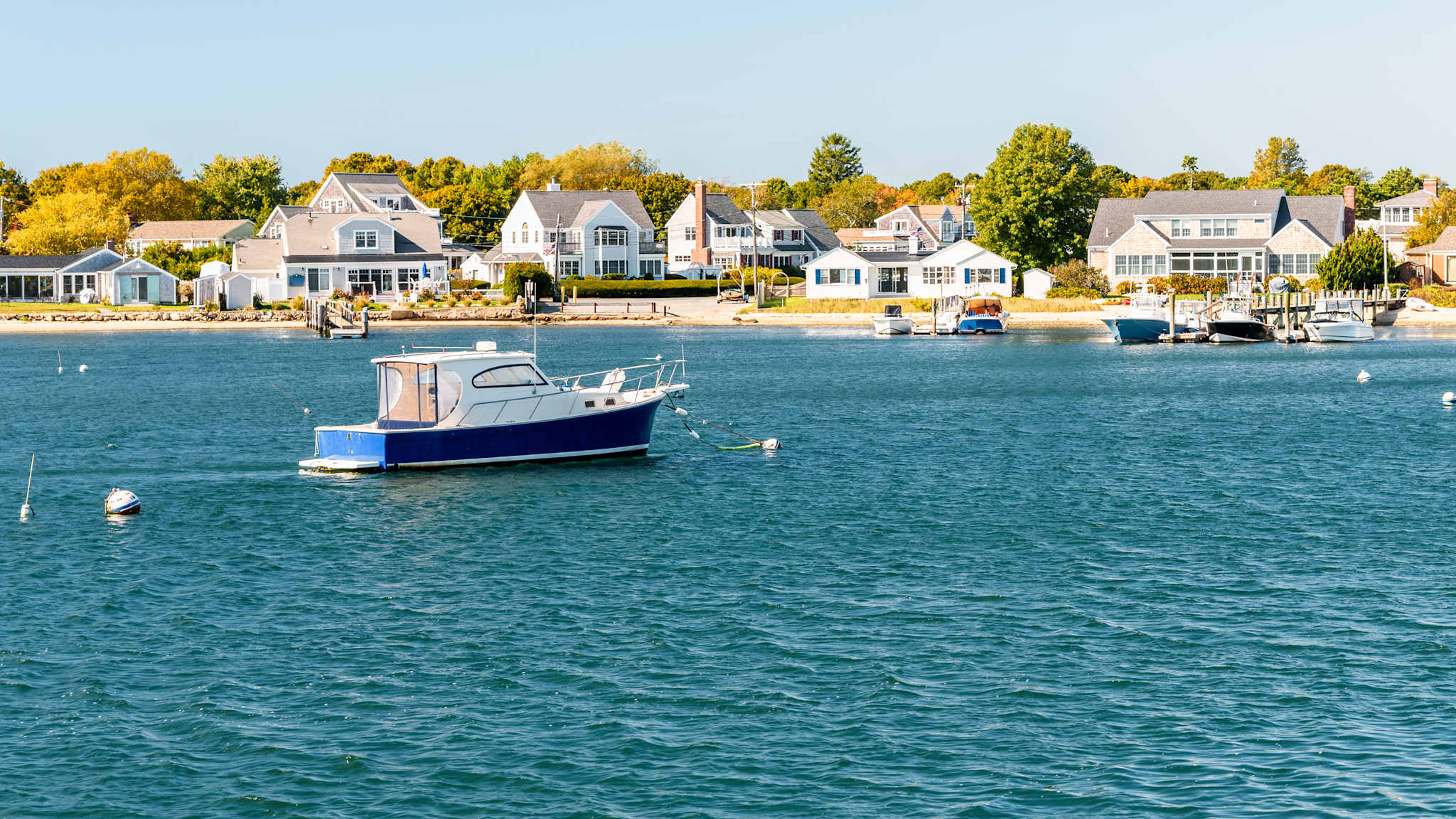 Ein Boot ist vor dem Strand von Hyannis, Cape Cod verankert, mit mehreren Häusern an der Küste im Hintergrund.