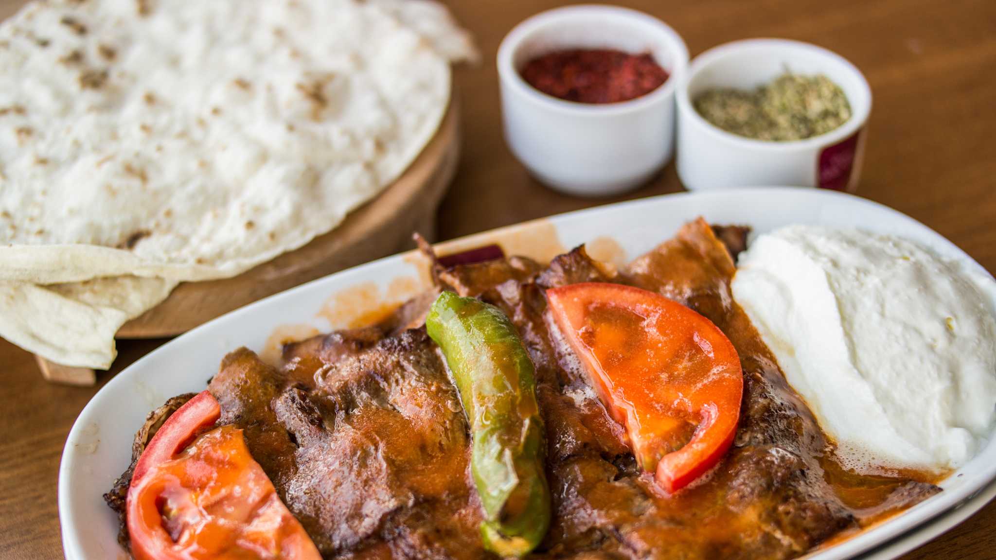 Teller mit Fleisch, Tomaten und Jogurt, im Hintergrund Fladenbrot und Gewürze in zwei kleinen Schalen