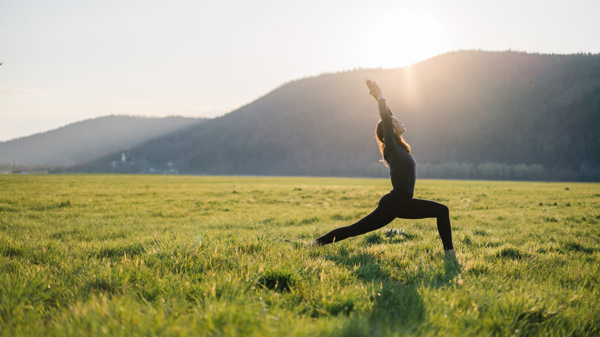 Junge Frau übt Yoga in grasbewachsener Wiese bei Sonnenaufgang © iStock.com/AscentXmedia