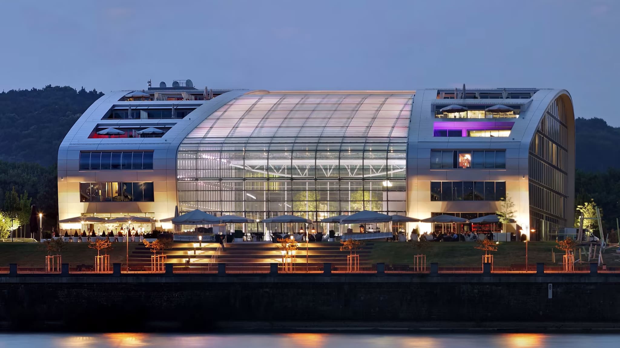 Glasfassade des Kameha Grand Hotels in Bonn bei Nacht, beleuchtet am Ufer des Rheins.