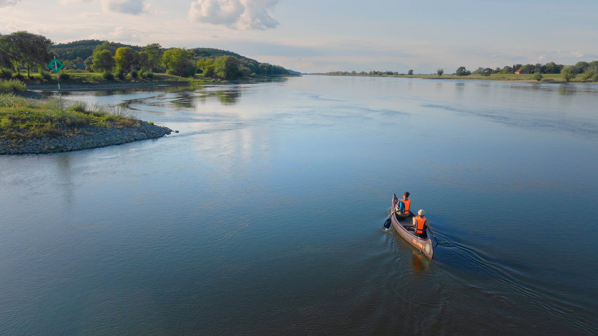Ein Kanu gleitet über die ruhige Elbe, während zwei Personen in orangefarbenen Schwimmwesten die weite Flusslandschaft und das Grün der Ufer genießen.