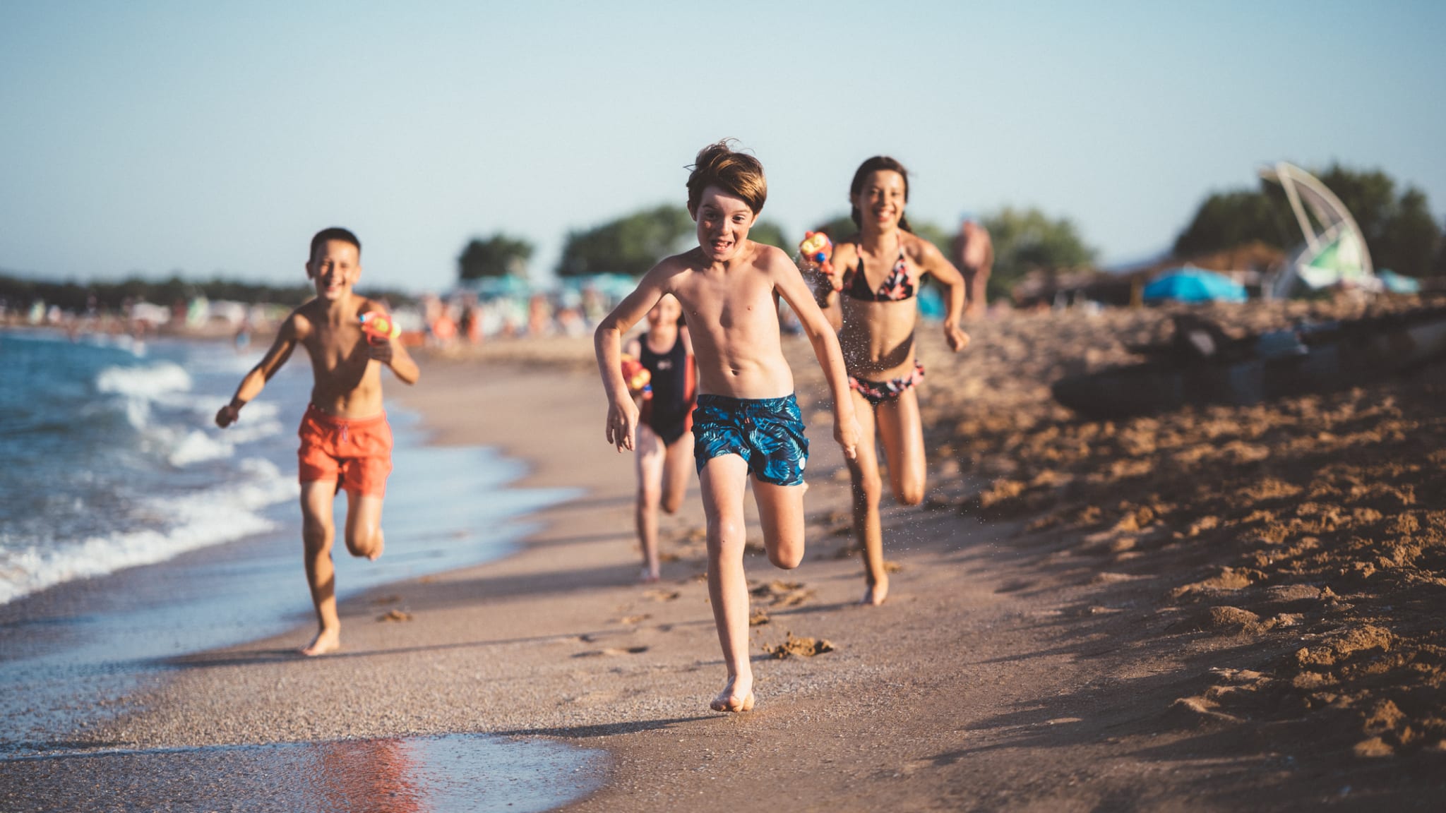 Kinder laufen und schießen mit Wasserpistolen am Strand © iStock.com/martin-dm