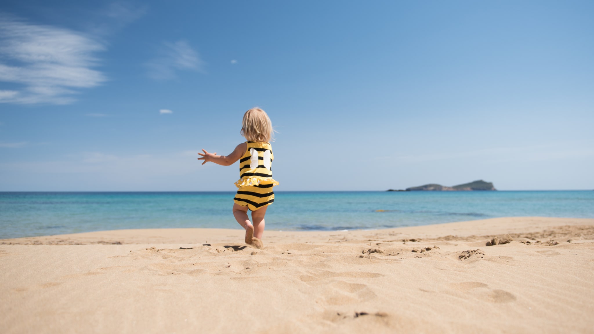 Kleines Mädchen rennt glücklich über einen Sandstrand im Urlaub © iStock.com/kamsta