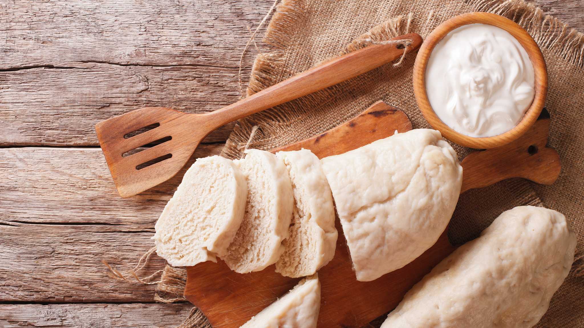 Es werden Scheiben von einer tschechischen Knedlíky Rolle auf einem Holzbrett abgeschnitten.